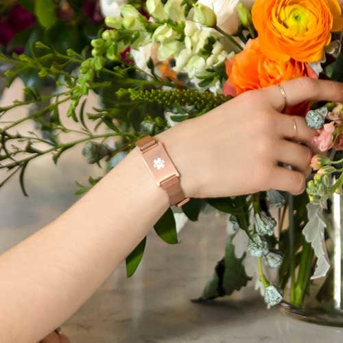 Woman touching flowers and wearing rose gold medical ID bracelet with mesh band