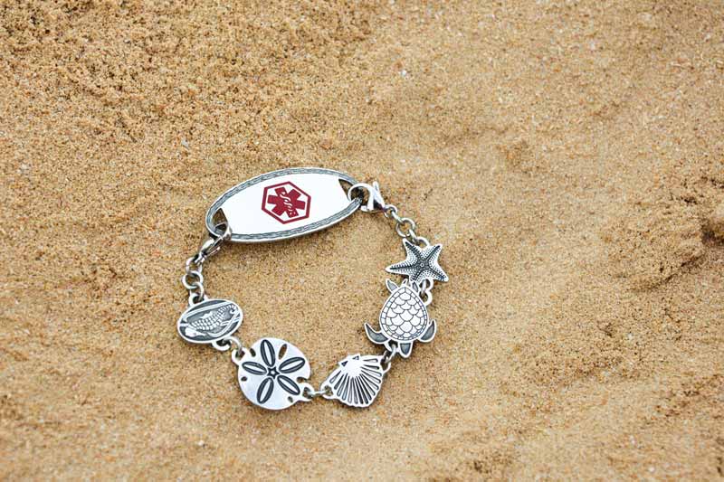 Silver medical ID bracelet in sand with red caduceus